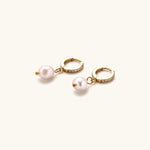 Load image into Gallery viewer, Gold huggie hoop earrings with pavé crystals and white freshwater pearl drops on cream background