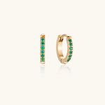 Load image into Gallery viewer, Pair of small gold huggie hoop earrings with bright green cubic zirconia stones on cream background