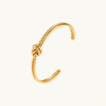 Load image into Gallery viewer, Gold cuff bracelet with twisted rope texture and decorative knot centerpiece on cream background.