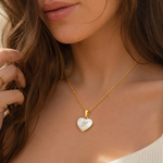 Load image into Gallery viewer, 18k Pearl Heart Initial Letter Necklace woman wearing a delicate gold chain with a heart pendant featuring a white inlay and gold M monogram.