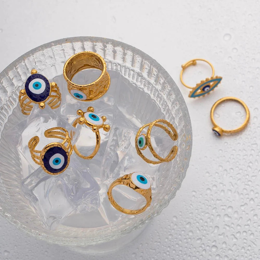 18k Bohemian Evil Eye Rings gold rings with blue eye designs displayed on a textured white surface.