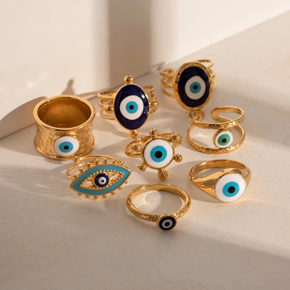 18k Bohemian Evil Eye Rings gold rings with blue eye designs displayed on a light surface.
