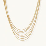 Load image into Gallery viewer, Seven delicate gold-plated snake chains create an elegant layered necklace on a neutral background.
