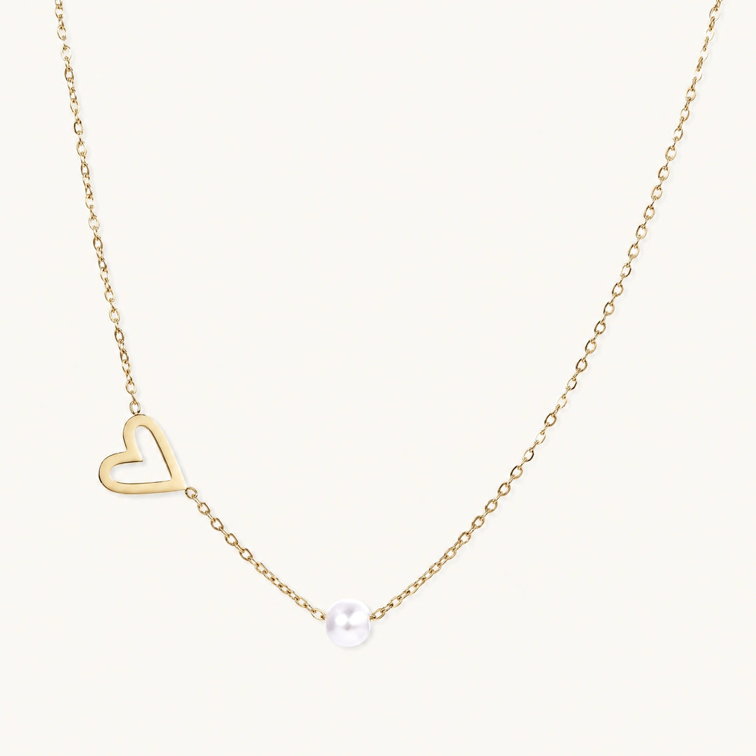 Dainty 14K gold plated stainless steel necklace with an open heart charm and a single round white bead on a cream background.