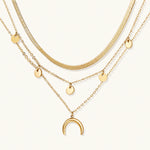 Load image into Gallery viewer, Four-layer gold necklace with herringbone chain, disc charms, and crescent moon pendant on cream background
