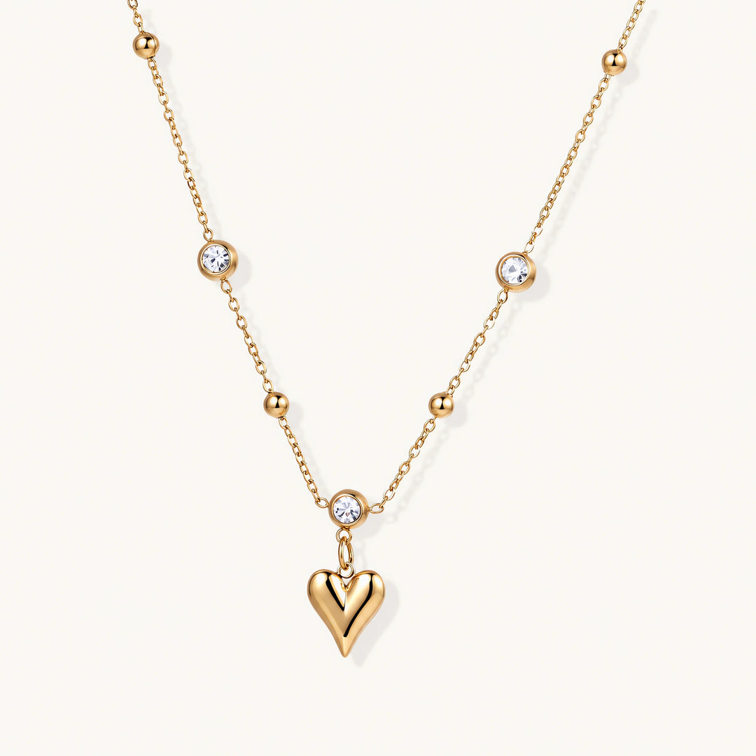 Delicate gold-plated necklace with bezel-set crystals and small heart pendant on beige background