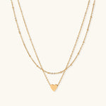 Load image into Gallery viewer, Delicate double-chain gold necklace with tiny heart pendant on cream background
