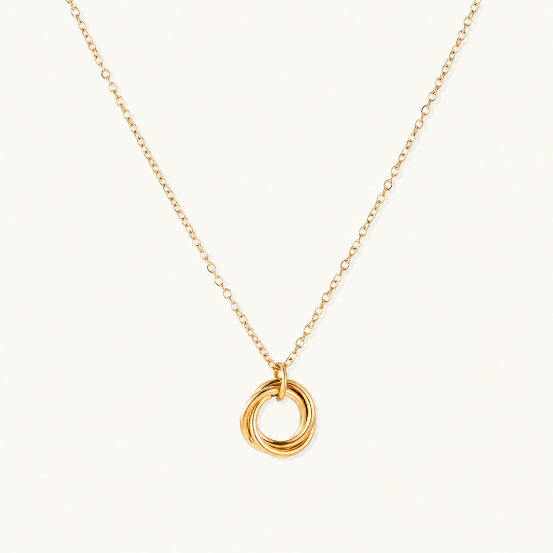 Delicate gold-plated necklace with three interlocking circle rings forming a minimalist knot pendant on cream background