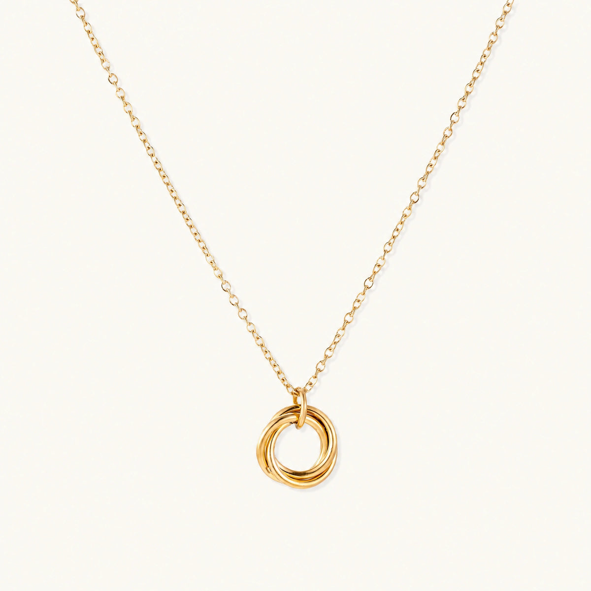 Delicate gold-plated necklace with three interlocking circle rings forming a minimalist knot pendant on cream background