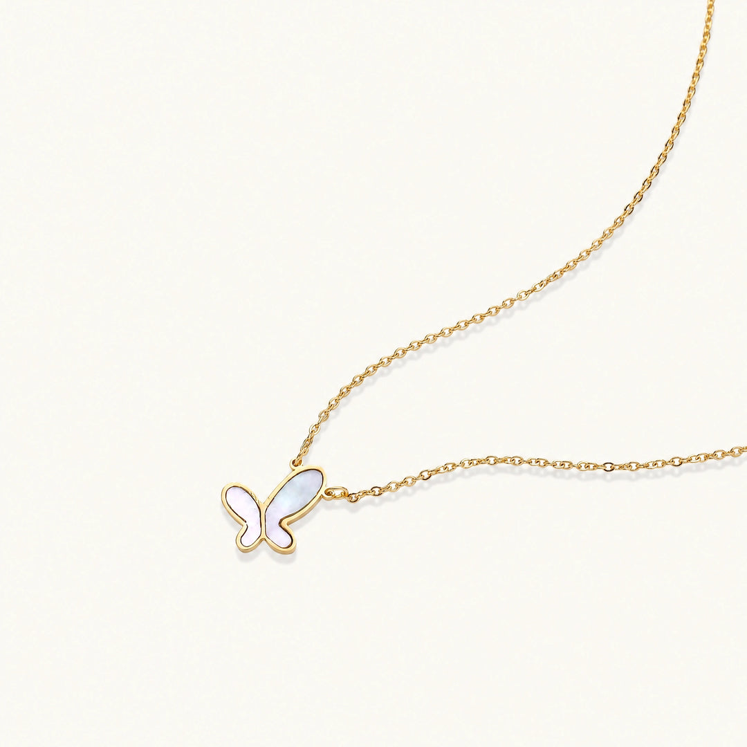 Gold-plated butterfly pendant with iridescent mother of pearl inlay on delicate chain against cream background.