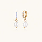 Load image into Gallery viewer, Gold huggie hoop earrings with pavé crystals and white freshwater pearl drops on cream background
