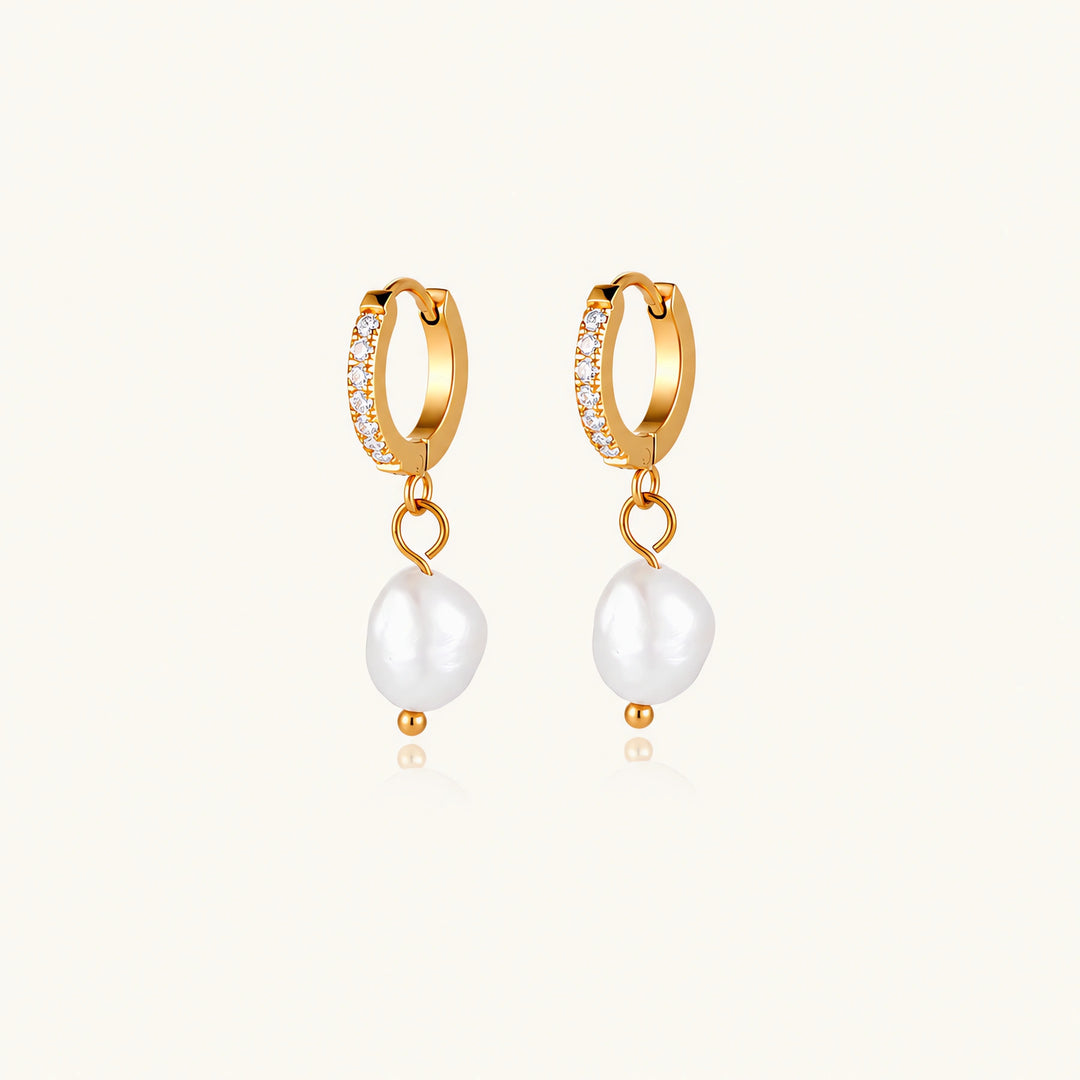 Gold huggie hoop earrings with pavé crystals and white freshwater pearl drops on cream background