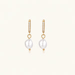 Load image into Gallery viewer, Gold huggie hoop earrings with pavé crystals and white freshwater pearl drops on cream background
