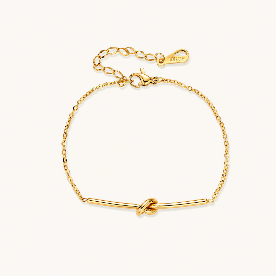 Delicate gold chain bracelet with minimalist bar and centered knot detail on cream background