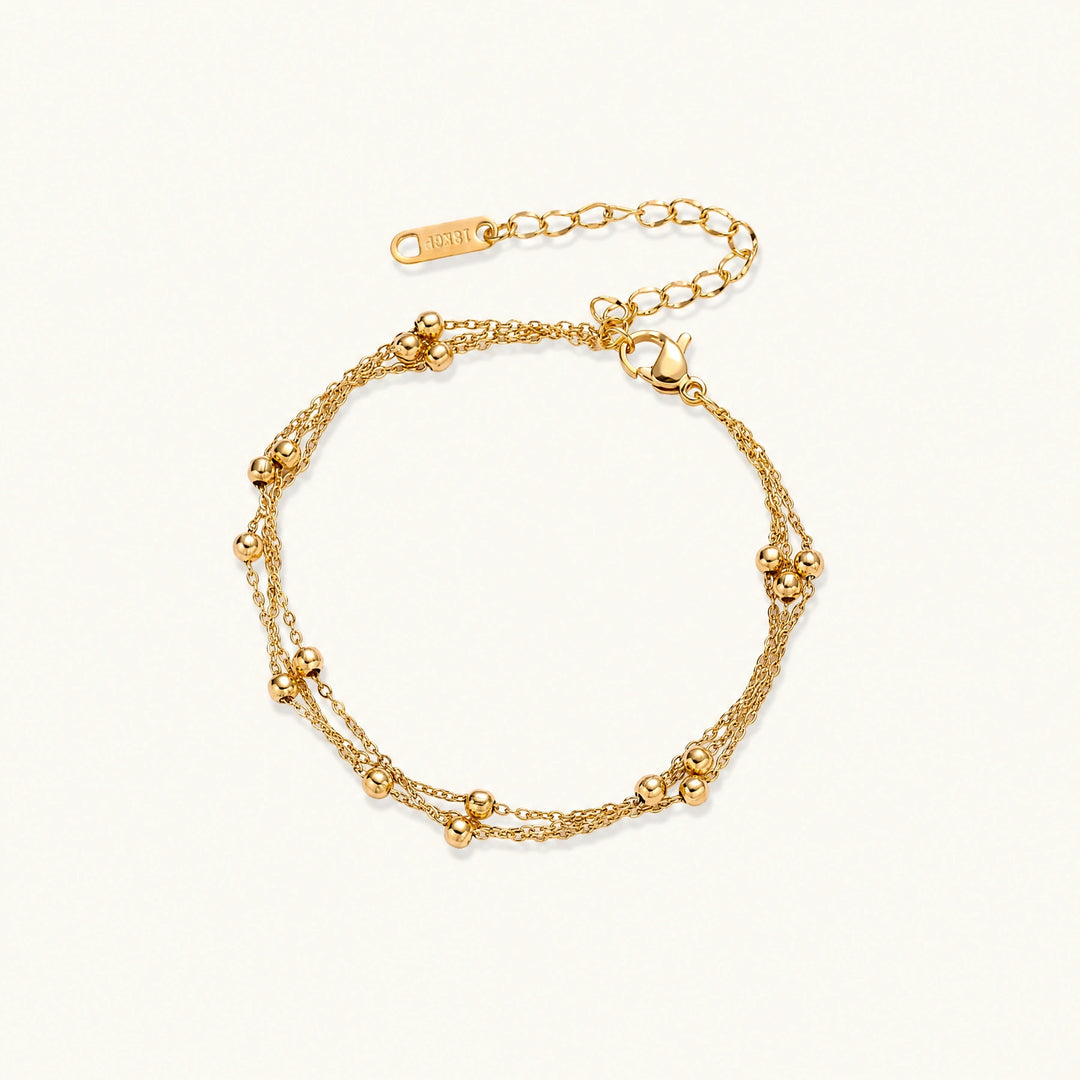 Three-strand gold-plated bracelet with clustered ball beads and adjustable clasp on cream background