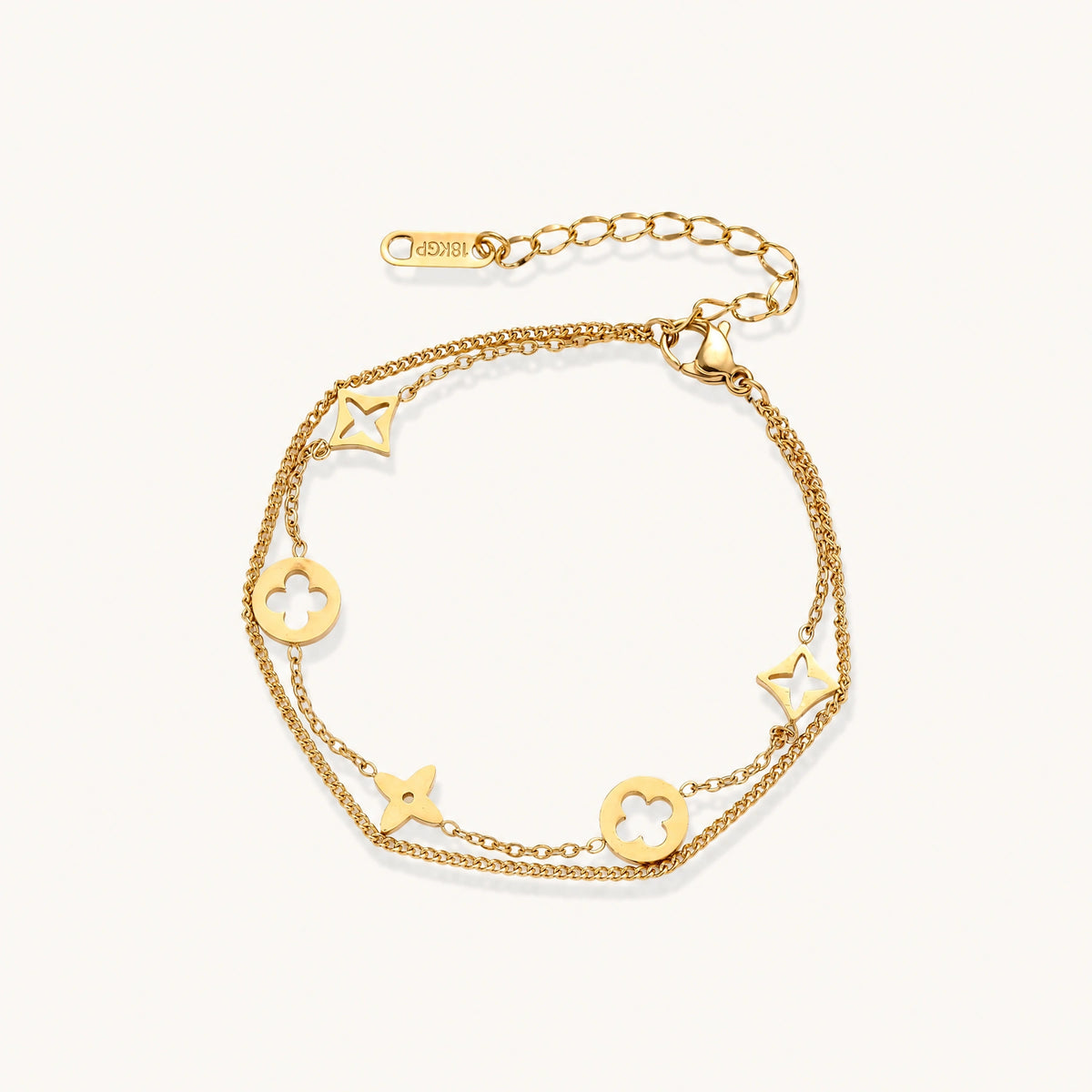 Double-layer gold-plated bracelet with quatrefoil and star charms on cream background, 18K gold finish.