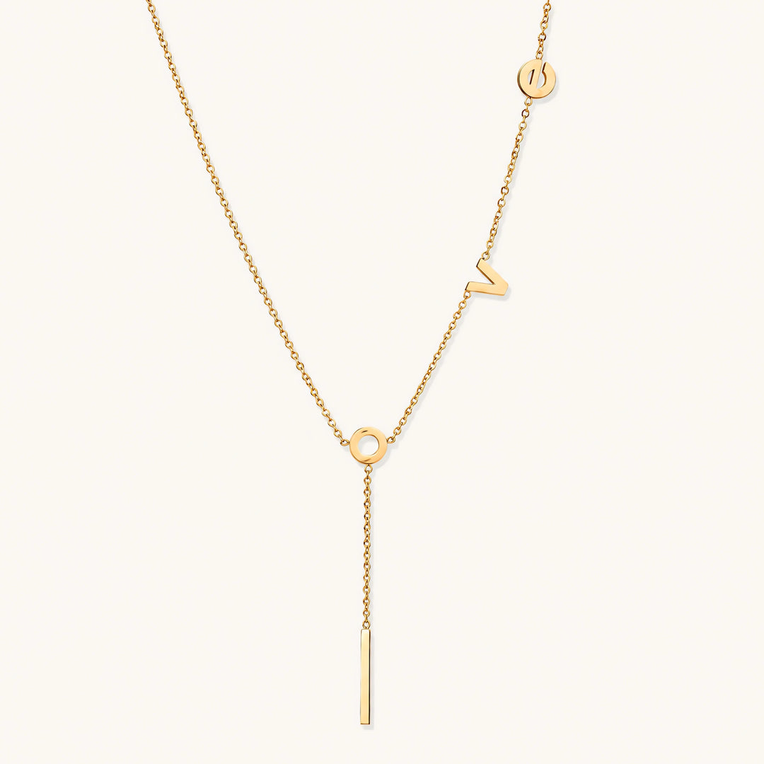 Gold Y-shaped necklace with L-O-V-E letter charms and vertical bar pendant on delicate chain against cream background