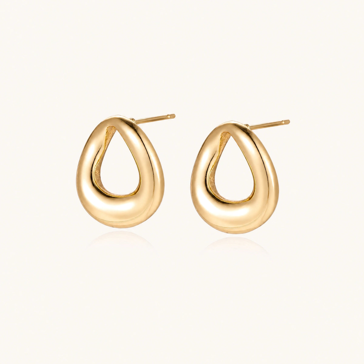 Pair of polished 18K gold-plated stainless steel teardrop earrings with hollow centers on cream background