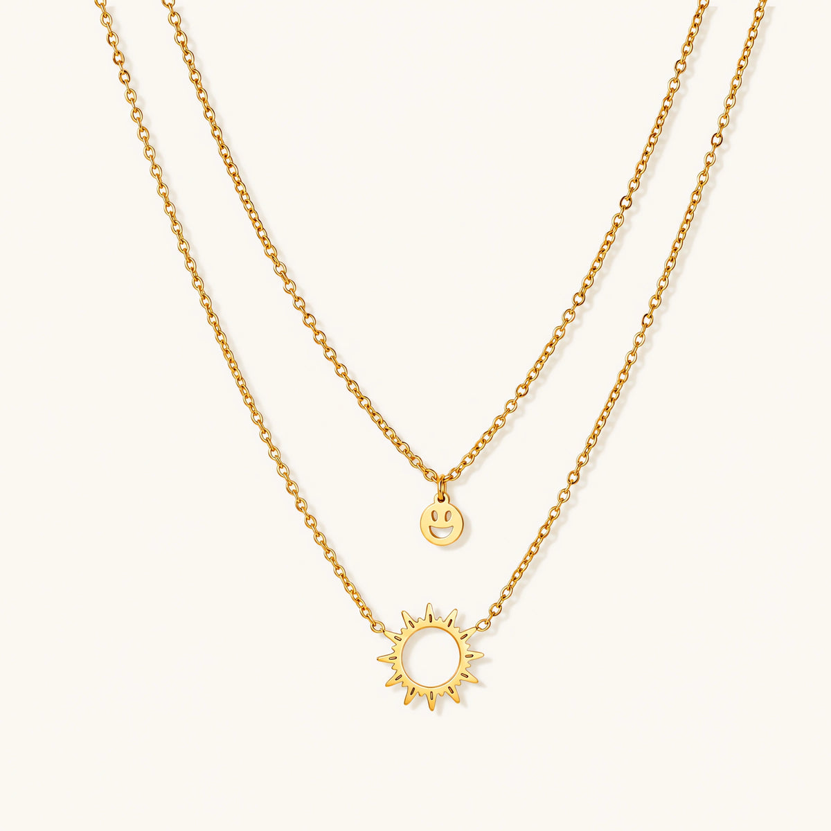 Gold layered necklace set with sunburst and smiley face pendants on delicate chains against white background.