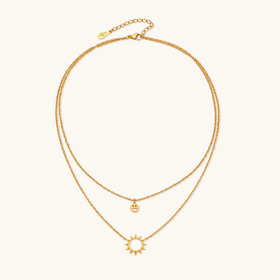 Gold layered necklace set with sunburst and smiley face pendants on delicate chains against white background.