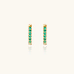 Load image into Gallery viewer, Pair of small gold huggie hoop earrings with bright green cubic zirconia stones on cream background
