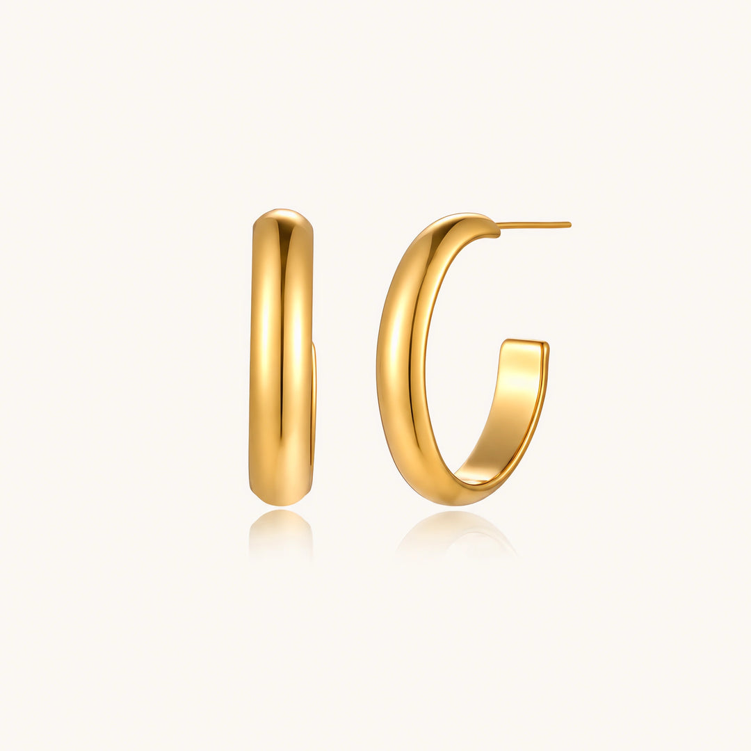 Chunky tubular hoop earrings in warm 14K gold-plated finish with smooth polished surface on cream background.