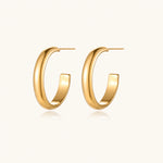 Load image into Gallery viewer, Chunky tubular hoop earrings in warm 14K gold-plated finish with smooth polished surface on cream background.
