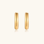 Load image into Gallery viewer, Chunky tubular hoop earrings in warm 14K gold-plated finish with smooth polished surface on cream background.
