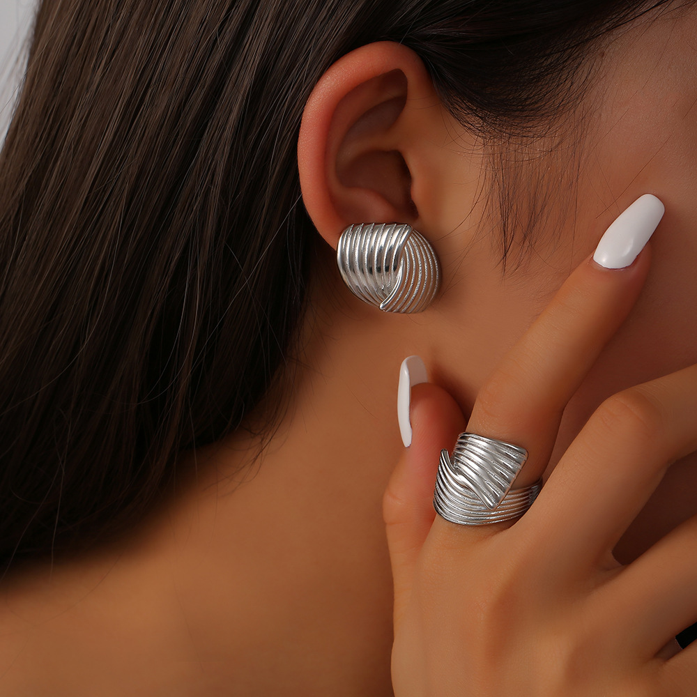 Sonia gold wave earrings silver earrings and ring worn by a person with dark hair and white nail polish