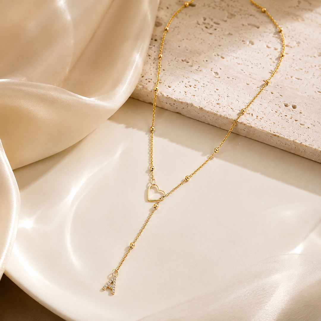 Dainty Diamond Letter Initial Lariat Necklace delicate gold Y-necklace with open heart and dangling A charm on a white ceramic plate.