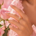 Load image into Gallery viewer, Rapunzel Crown Inspired Necklaces and Rings woman's hand wearing a delicate gold ring with a white floral cluster against a soft pink floral background.

