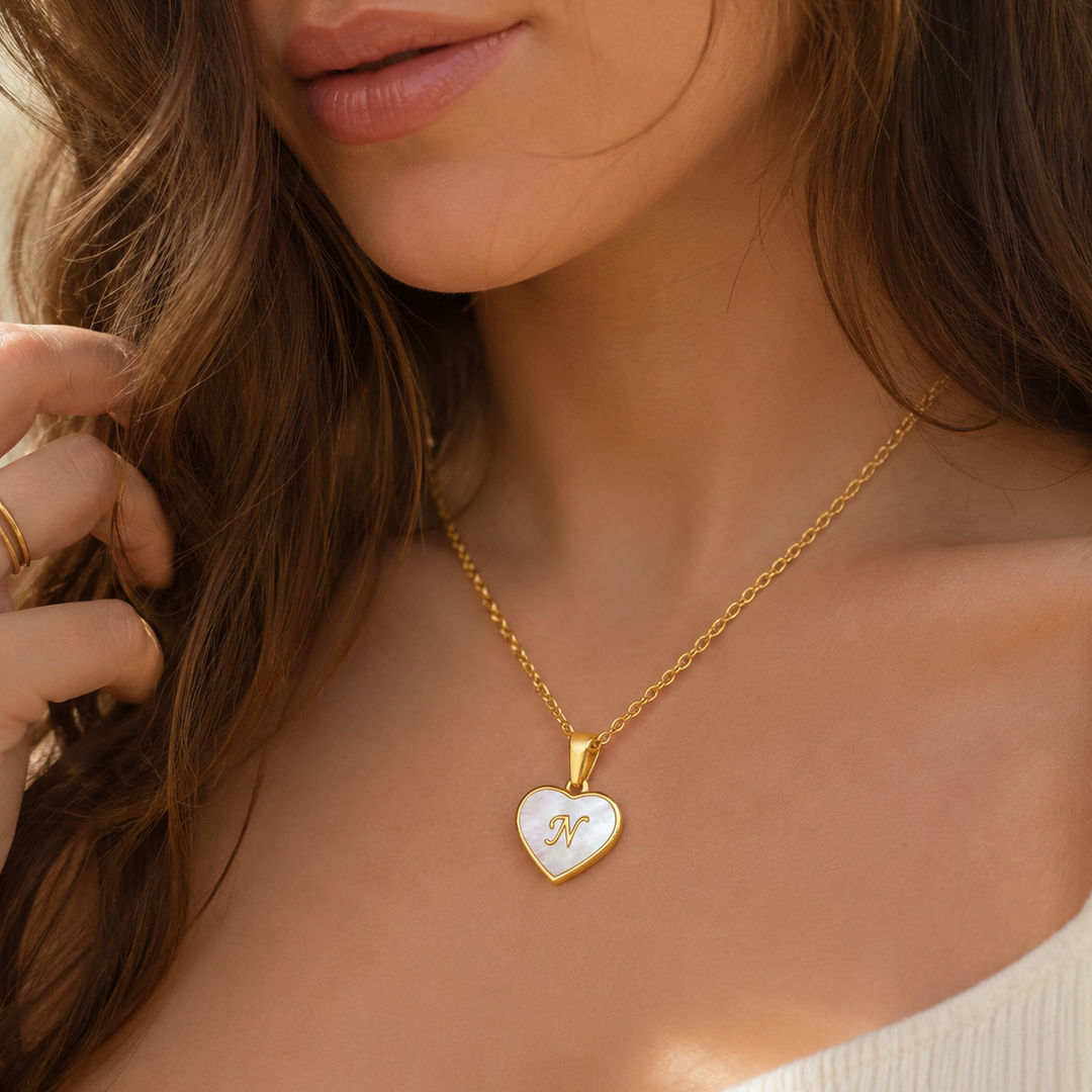 18k Pearl Heart Initial Letter Necklace woman wearing a delicate gold chain with a heart pendant featuring a white inlay and gold M monogram.