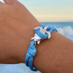 Load image into Gallery viewer, Elegant Sea Turtle Bracelet blue braided bracelet with silver anchor charm worn on a wrist against a beach background.
