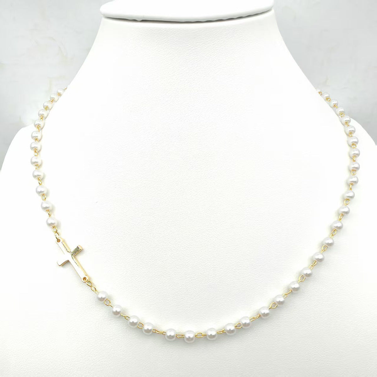 Dainty Faux Pearl Cross Station Choker Necklace pearl necklace with gold accents displayed on a mannequin neck against a white background.