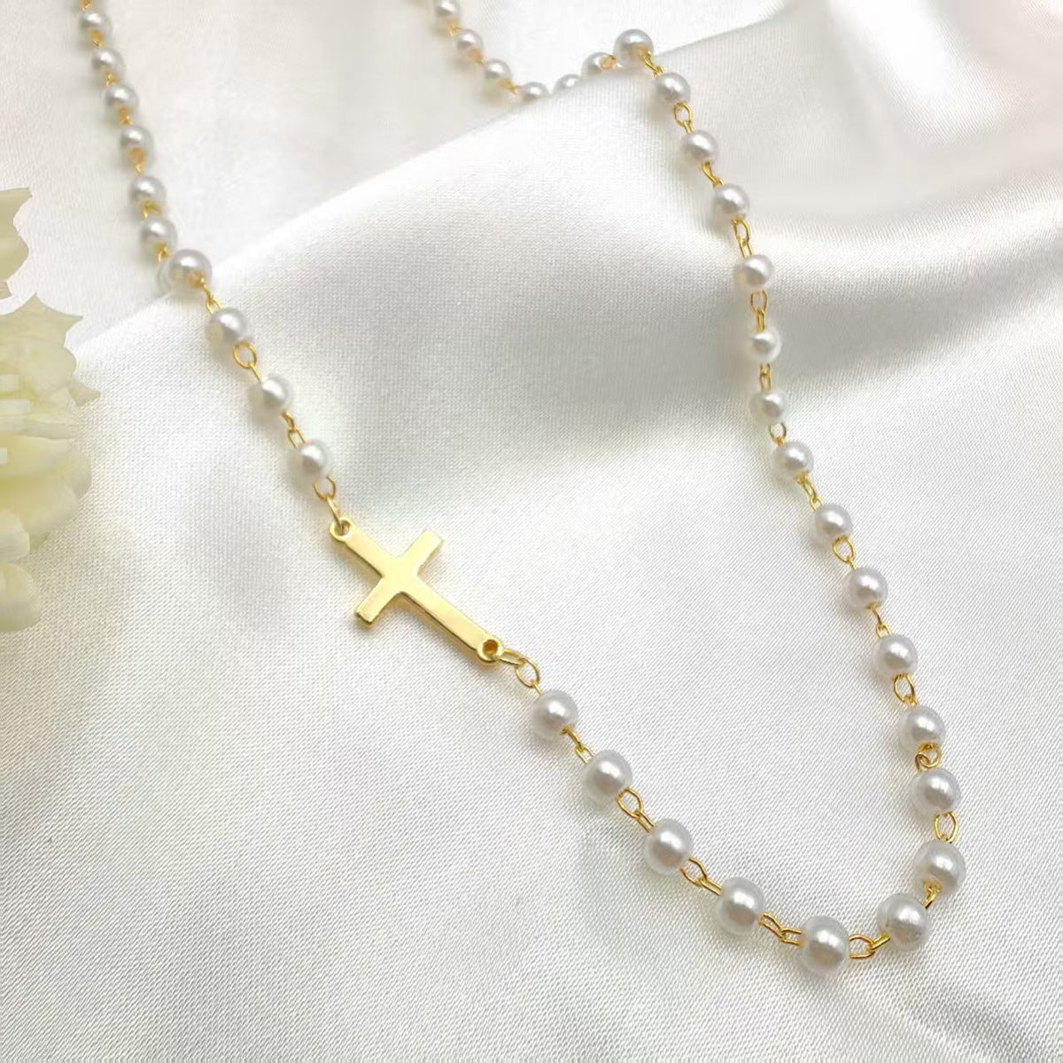 Dainty Faux Pearl Cross Station Choker Necklace pearl necklace with a gold cross pendant displayed on a white fabric background.