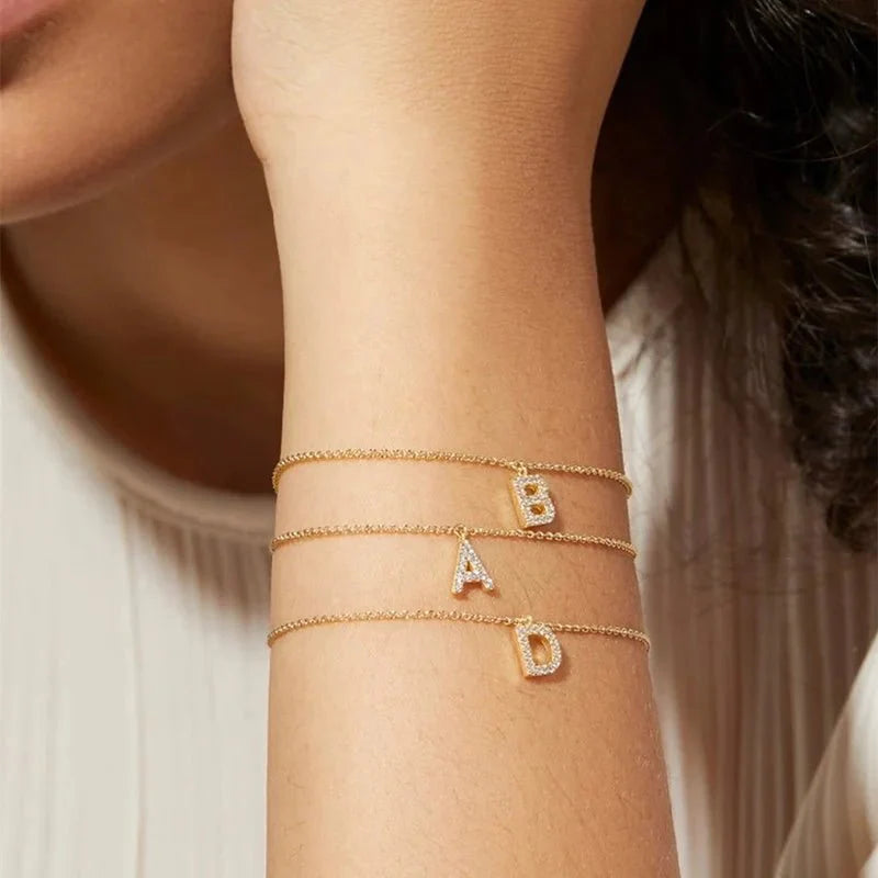 Dainty chain diamond initial bracelet gold bracelet with letter charms worn on a wrist against a neutral background