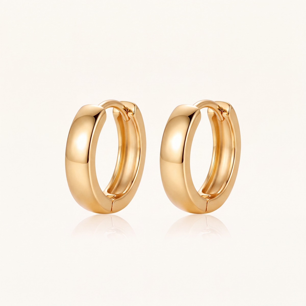 Pair of minimalist gold huggie hoop earrings on a cream background